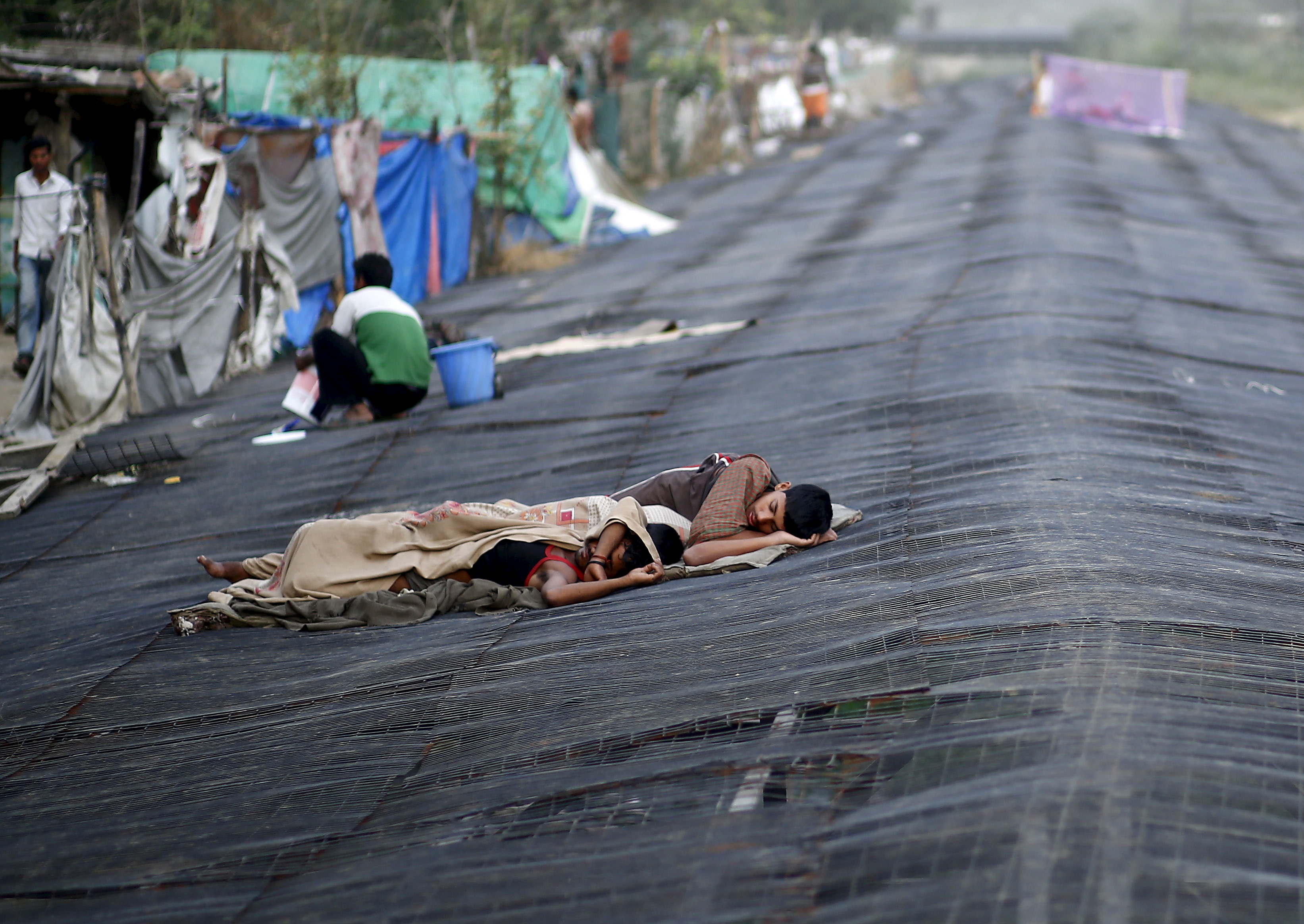 Men sleep on a temporary shade built over a drain next to a slum in New Delhi, India, May 28, 2015. Photo by Anindito Mukherjee/Reuters
