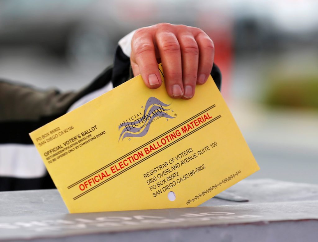 A poll worker places a mail in ballot into a voting box as voters drop off their ballot in the U.S. presidential primary e...
