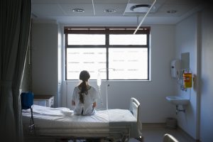 Patient sitting on hospital bed waiting for surgery looking out window. Photo by Portra Images/via Getty Images
