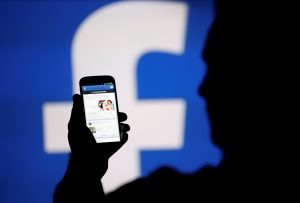 A man is silhouetted against a video screen with a Facebook logo as he poses with a Samsung S4 smartphone in this photo illustration taken in the central Bosnian town of Zenica, August 14, 2013. REUTERS/Dado Ruvic/File Photo - RTSUXXI