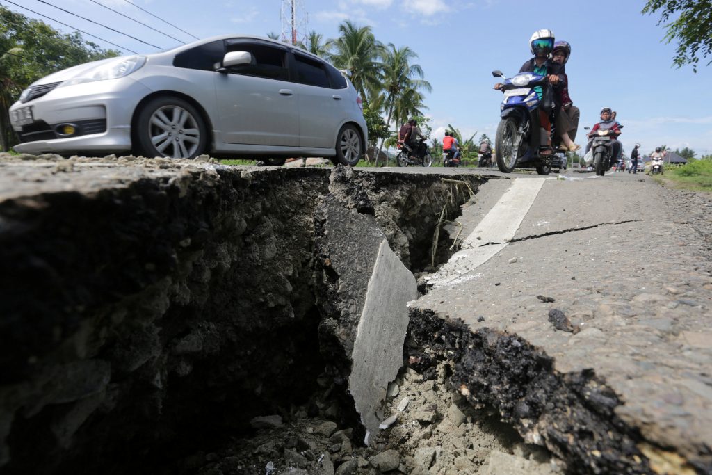 Motorcyclists pass a damaged section of a road following a Dec. 7 earthquake in Meuredu, Pidie Jaya, in the northern province of Aceh, Indonesia.  Antara Foto/Irwansyah Putra/via REUTERS