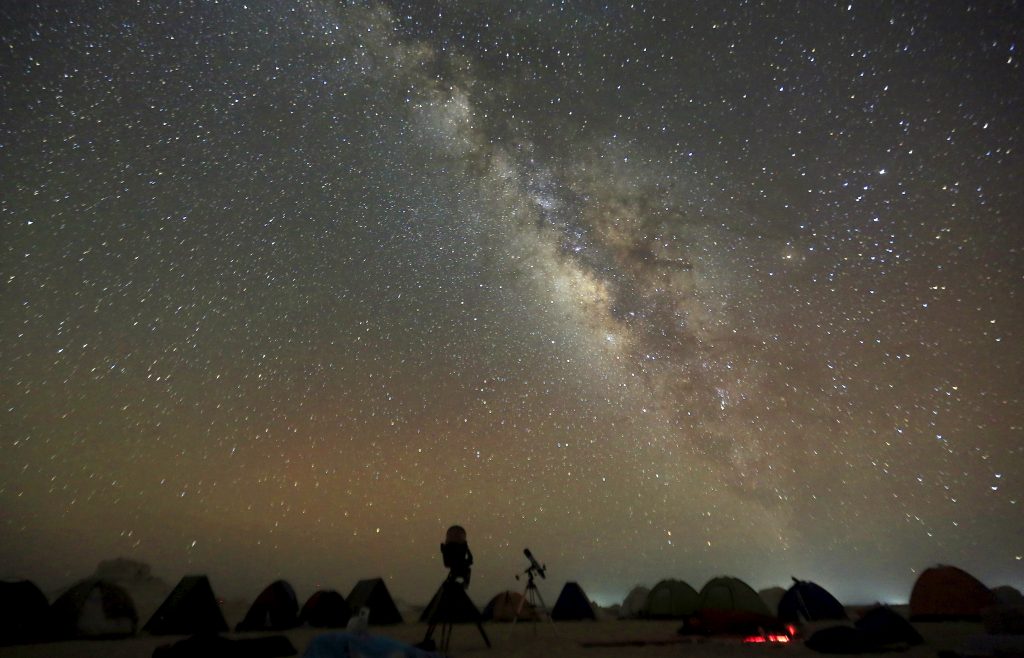 The 'Milky Way' is seen in the night sky around telescopes and camps of people over rocks in the White Desert north of the...
