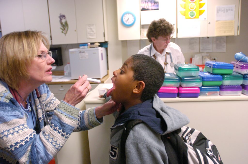 A nurse checks 9-year-old's throat while checking in for his daily medications and lung test at the Kunsberg School in Den...