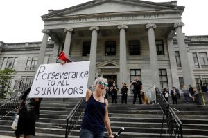 Bird Milliken weeps as she carries a sign while demonstrating in support of victims of sexual violence after a judge declared a mistrial in his sexual assault trial at the Montgomery County Courthouse in Norristown, Pennsylvania