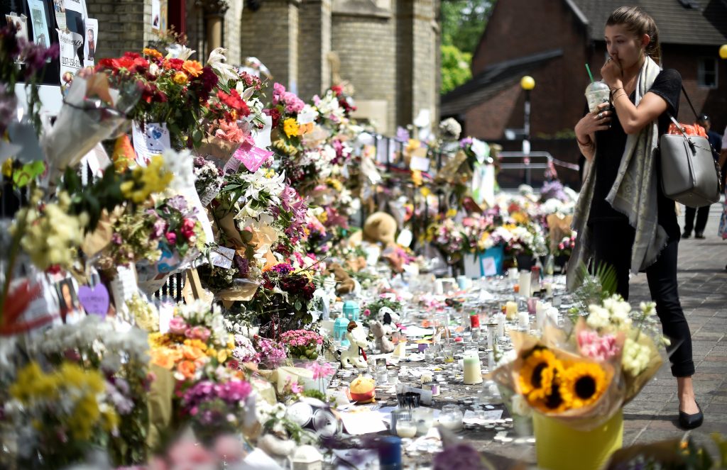 A woman looks at flowers, tributes and messages left for the victims of the fire at the Grenfell apartment tower in North Kensington