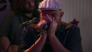 Marcus Oglesby plays harmonica with his band, Creek Don't Rise, and sings "White Coat Man," a song he wrote in response to the mark opioids left on his hometown in West Virginia. Photo by Abbey Oldham