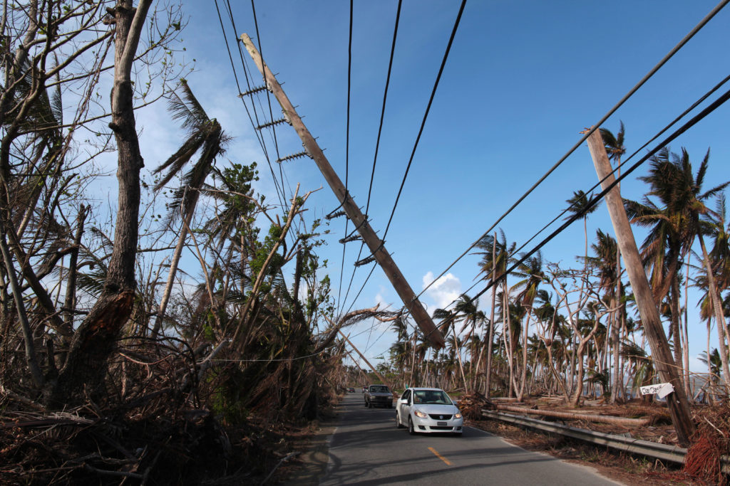 Cars drive under a partially collapsed utility pole, after the island was hit by Hurricane Maria in September, in Naguabo,...