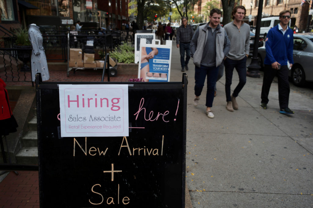 FILE PHOTO: Pedestrians pass a sign advertising a sale and a job opening at a shop on Newbury Street in Boston, Massachuse...