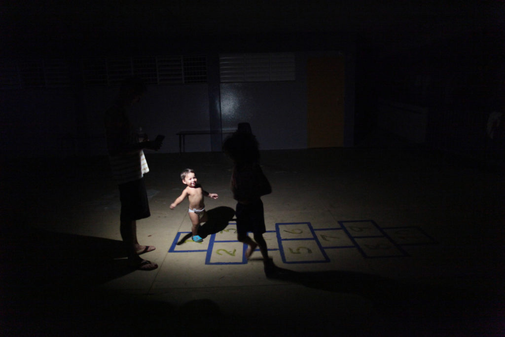 Children play in the light of a flashlight at a school turned shelter, after their home was destroyed when Hurricane Maria...