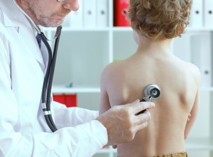 Old male doctor examining a child patient by stethoscope. Health care concept.