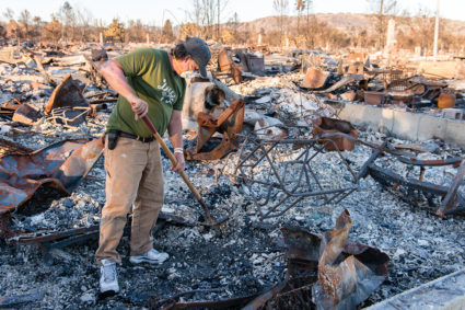 Ed Corn wears a mask as he sifts through the ashes of the home he shared with his paraplegic roommate in Santa Rosa’s Coffey Park neighborhood. “I can definitely taste the toxins in my throat and the back of my tongue,” he said. Photo by Heidi de Marco/KHN