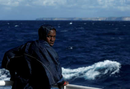 A migrant stands on the deck of the MV Aquarius, a search and rescue ship run in partnership between SOS Mediterranee and Medecins Sans Frontieres, as it passes the Maltese island of Gozo while making its way to the Italian island of Sicily after rescue operations in the central Mediterranean off the coast of Libya, December 17, 2017. Photo by Darrin Zammit Lupi/REUTERS