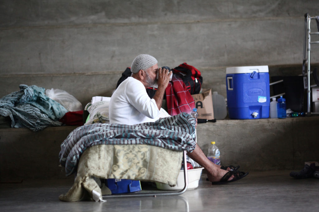 A man who lost his home during Hurricane Maria in September drinks a beverage while sitting on a cot at a school turned sh...