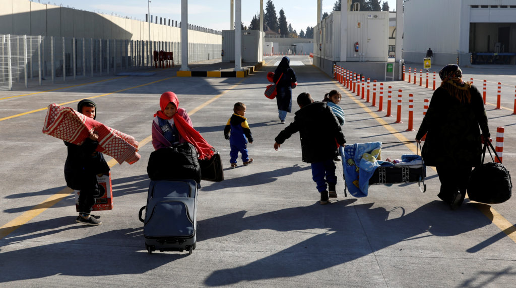 A Syrian woman carries a cradle with his son as she and her children walk through the border gate to cross into the Syrian...