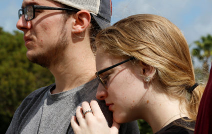 Former Marjory Stoneman Douglas High School student Madisyn Coles leans on the shoulder of an unidentified friend as they view memorials on a fence surrounding the school in Parkland, Florida, U.S., February 23, 2018. REUTERS/Joe Skipper - RC13D1F70000