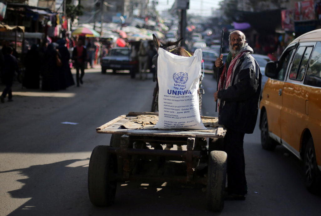 A Palestinian man stands next to a cart carrying a flour sack distributed by the United Nations Relief and Works Agency (U...