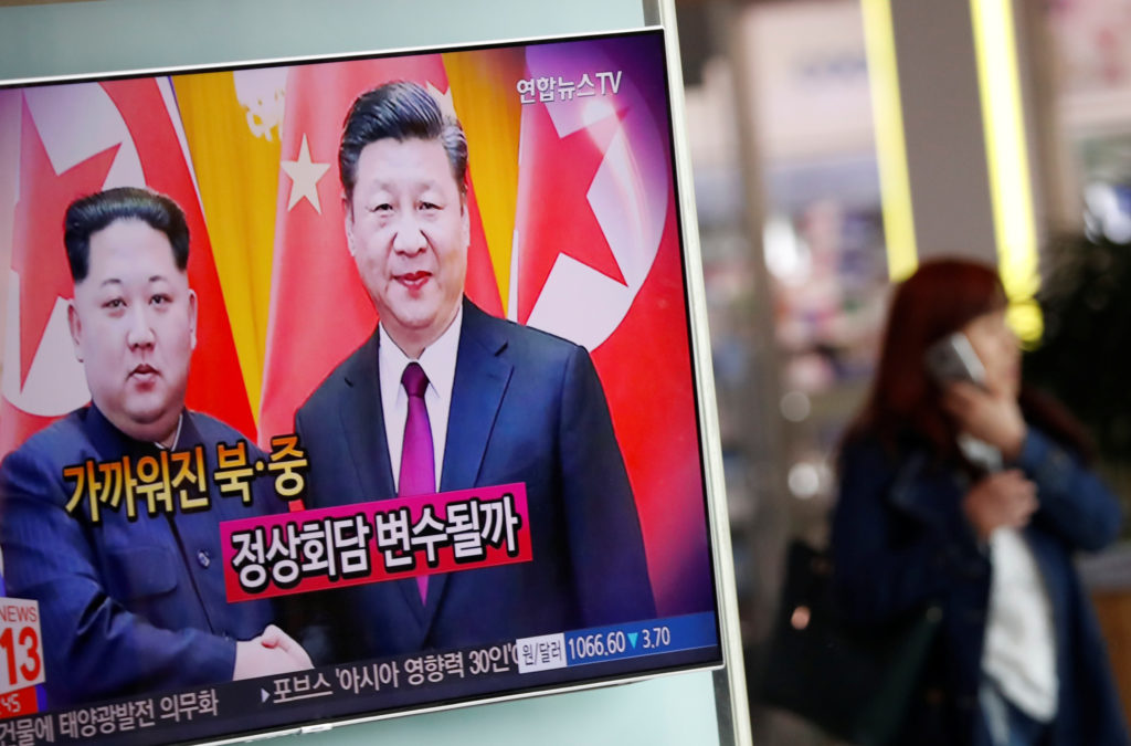A woman walks past a TV broadcasting a news report on a meeting between North Korean leader Kim Jong Un and Chinese Presid...