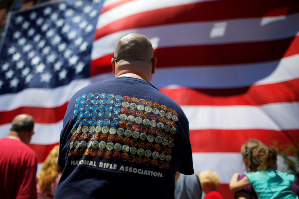 Onlookers, including a man wearing a National Rifle Association (NRA) t-shirt, watch as a 95-by-50-foot American flag is u...