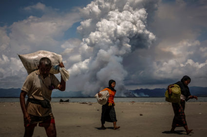 Smoke is seen on the Myanmar border as Rohingya refugees walk on the shore after crossing the Bangladesh-Myanmar border by boat through the Bay of Bengal, in Shah Porir Dwip, Bangladesh. Photo by Danish Siddiqui/Reuters