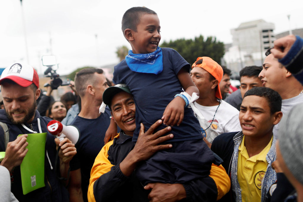 A man and his son, members of a caravan of migrants from Central America, react near the San Ysidro checkpoint as the first fellow migrants entered U.S. territory to seek asylum on Monday, in Tijuana, Mexico April 30, 2018. REUTERS/Edgard Garrido - RC1842479C70