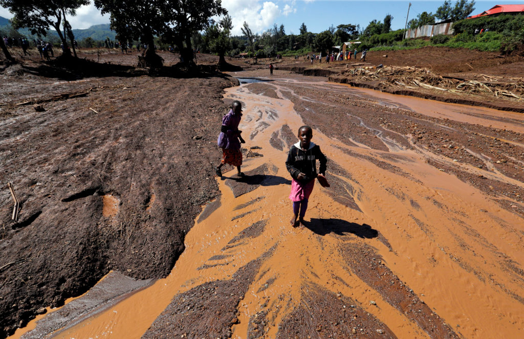 Children walk in muddy waters after a dam burst, which unleashed water at nearby homes, in Solio, a town near Nakuru, Keny...