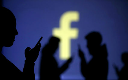 Silhouettes of mobile users are seen next to a screen projection of Facebook logo in this picture illustration taken March 2018. Photo by Dado Ruvic/Reuters