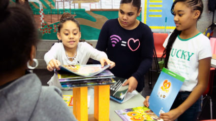 Janiyah Cruz, 9, and her friends pile magazines on paper pillars to see how much weight they can hold as part of a lesson by the Salvadori Center. Photo by Larisa Epatko/PBS NewsHour
