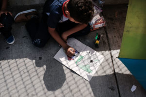 A Honduran child works in a coloring book while waiting with his family along the border bridge after being denied entry from Mexico into the U.S. on June 25 in Brownsville, Texas. Photo by Spencer Platt/Getty Images