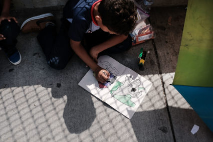 A Honduran child works in a coloring book while waiting with his family along the border bridge after being denied entry from Mexico into the U.S. on June 25 in Brownsville, Texas. Photo by Spencer Platt/Getty Images