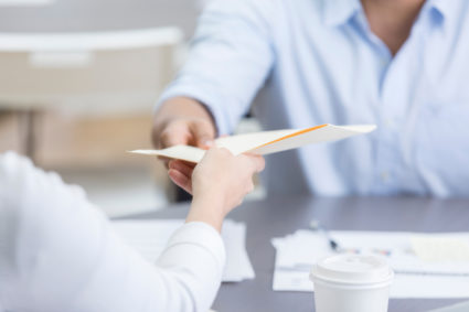 Closeup of two coworkers passing folder across table