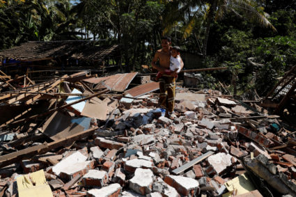 A man holds his child as he walks through the ruins of their house at Kayangan district after earthquake hit on Sunday in North Lombok, Indonesia, August 7, 2018. Photo by Beawiharta/Reuters.