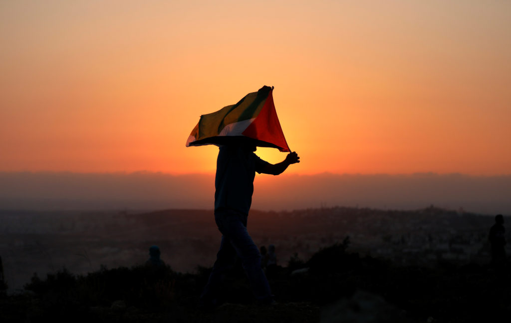 A demonstrator holds a Palestinian flag during a protest against Jewish settlements in the village of Ras Karkar, near Ram...