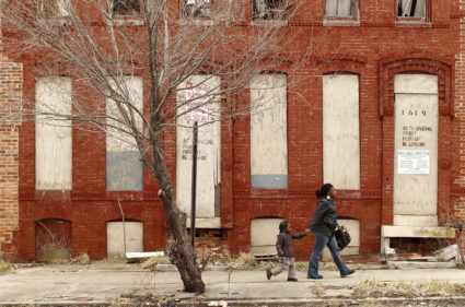 A woman and child walk past a dilapidated building in a run-down neighborhood of Baltimore, Maryland. New research suggests that impoverished Americans are getting left out even when their communities enjoy hiring booms. Photo by Kevin Lamarque/Reuters