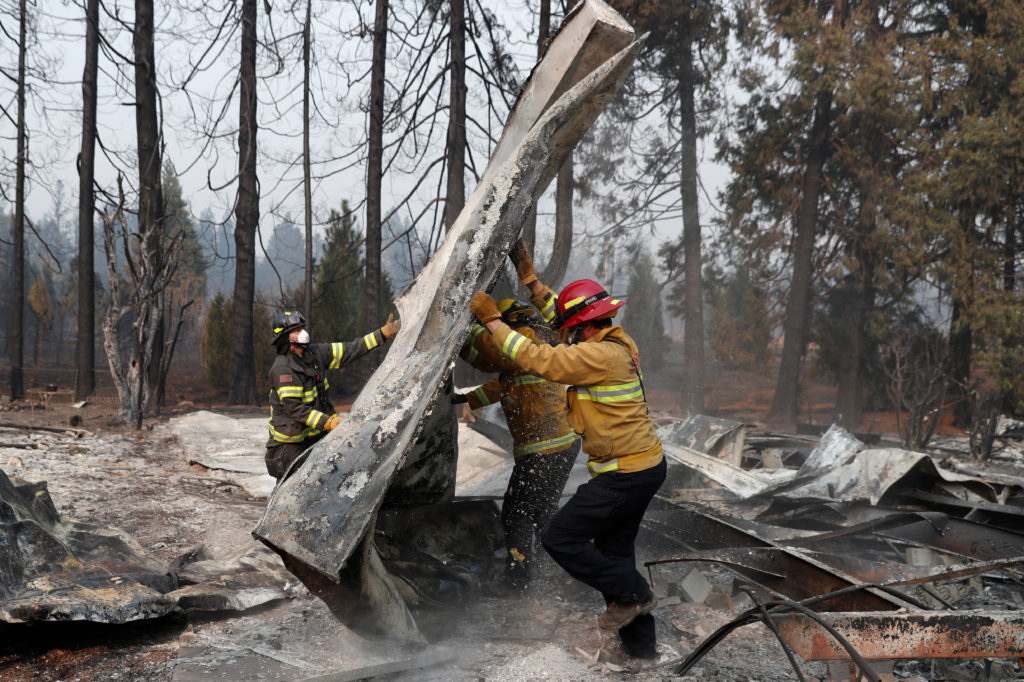 Firefighters move debris while recovering human remains from a trailer home destroyed by the Camp Fire in Paradise, Califo...