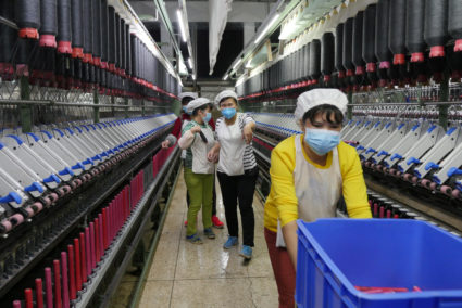 A worker jokes and beckons at her colleague as she rolls away carts of unused tools between rows of spinning machine at a factory owned by Hong Kong's Novetex Textiles Limited in Zhuhai City, China, in 2016. Photo by Venus Wu/Reuters