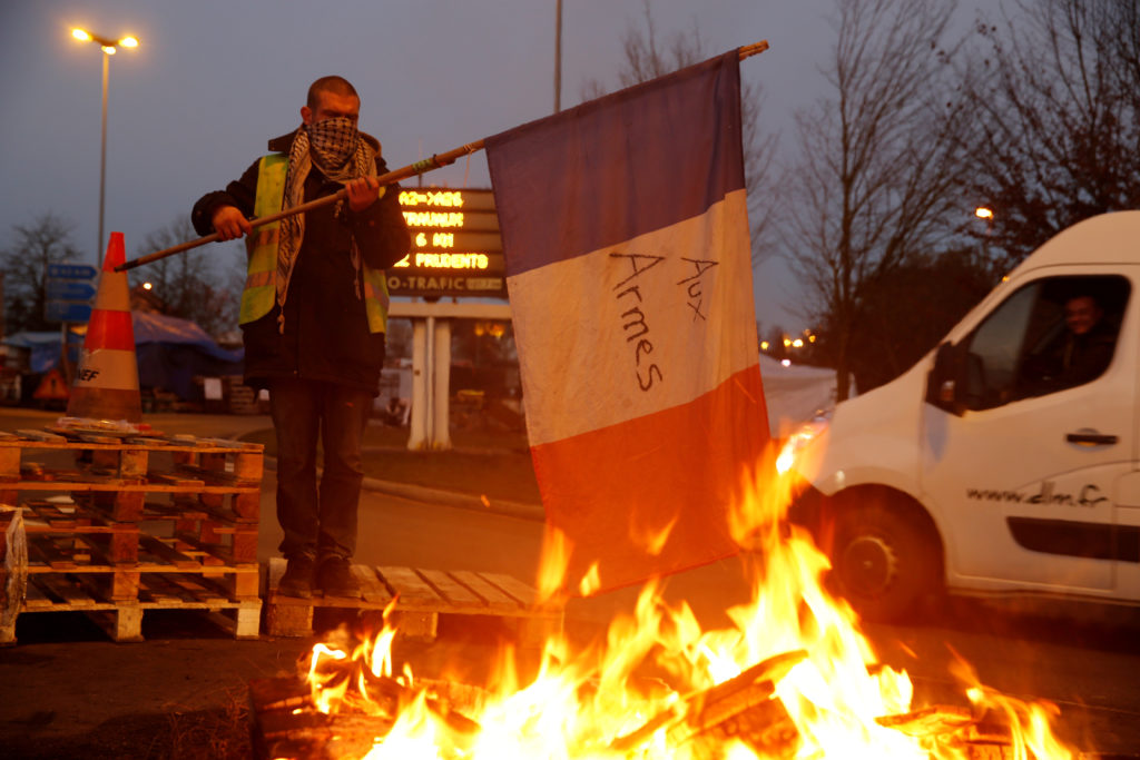 A protester wearing a yellow vest, the symbol of a French drivers' protest against higher diesel fuel prices, holds a flag...
