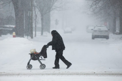 A man pushes a stroller with groceries as flurries swirl around on Woodward Ave. in Detroit, Michigan. Photo by Ryan Garza/Detroit Free Press/TNS via Getty Images