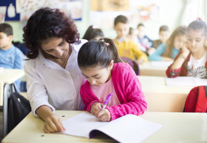 Teacher teaches to write to the girl student in the class