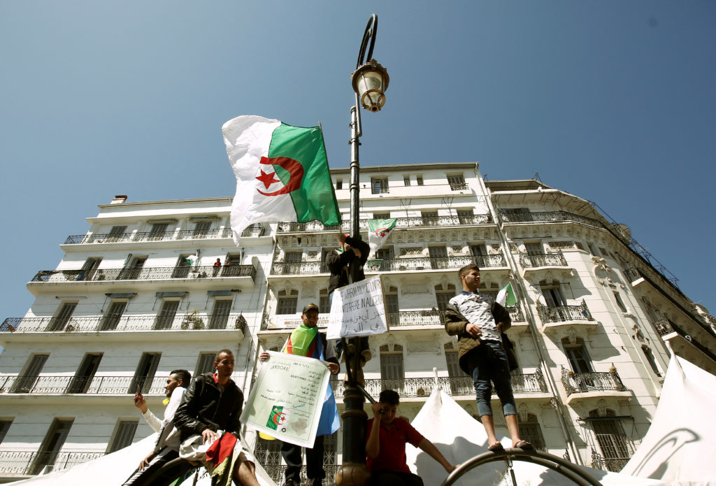 A demonstrator holds a national flag while standing on a street pole during a protest to demand the removal of President A...