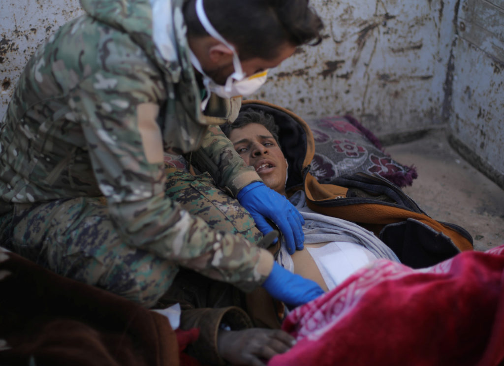 A member of the Syrian Democratic Forces (SDF) delivers care to Hareth Najem, an Iraqi orphan, near the village of Baghouz...