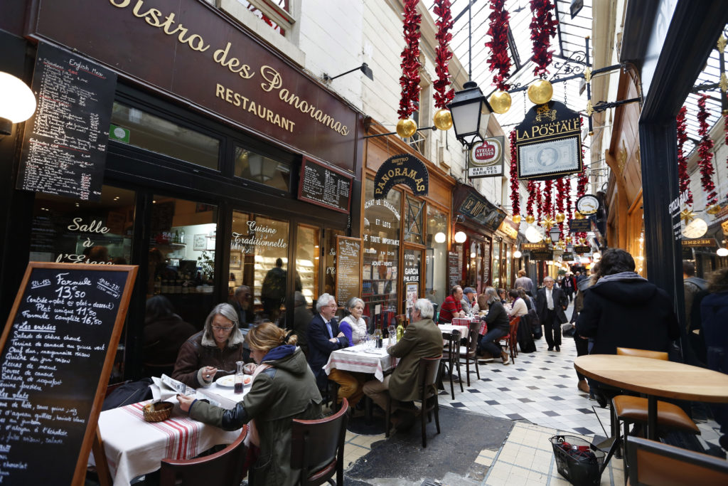 People sit at tables as they have lunch outside bistros in a covered passageway, the Passage des Panoramas, in Paris, Fran...