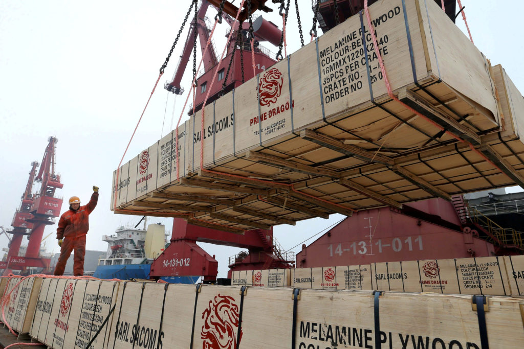 A worker gestures as a crane lifts goods for export onto a cargo vessel at a port in Lianyungang, Jiangsu province, China ...
