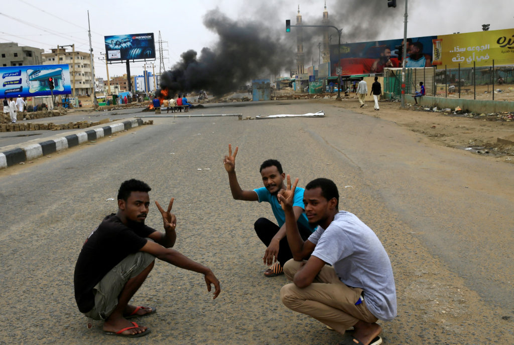 Sudanese protesters gesture as they sit-in near a barricade on a street, demanding that the country's Transitional Militar...