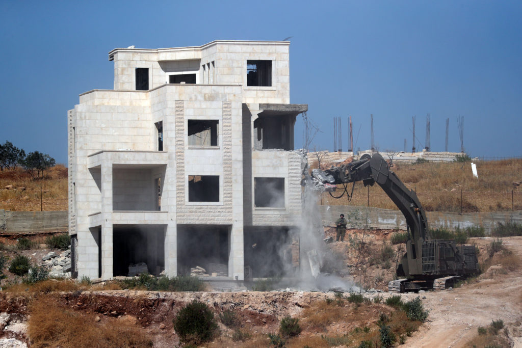 An Israeli military bulldozer demolishes a building near a military barrier in Sur Baher, a Palestinian village on the edg...