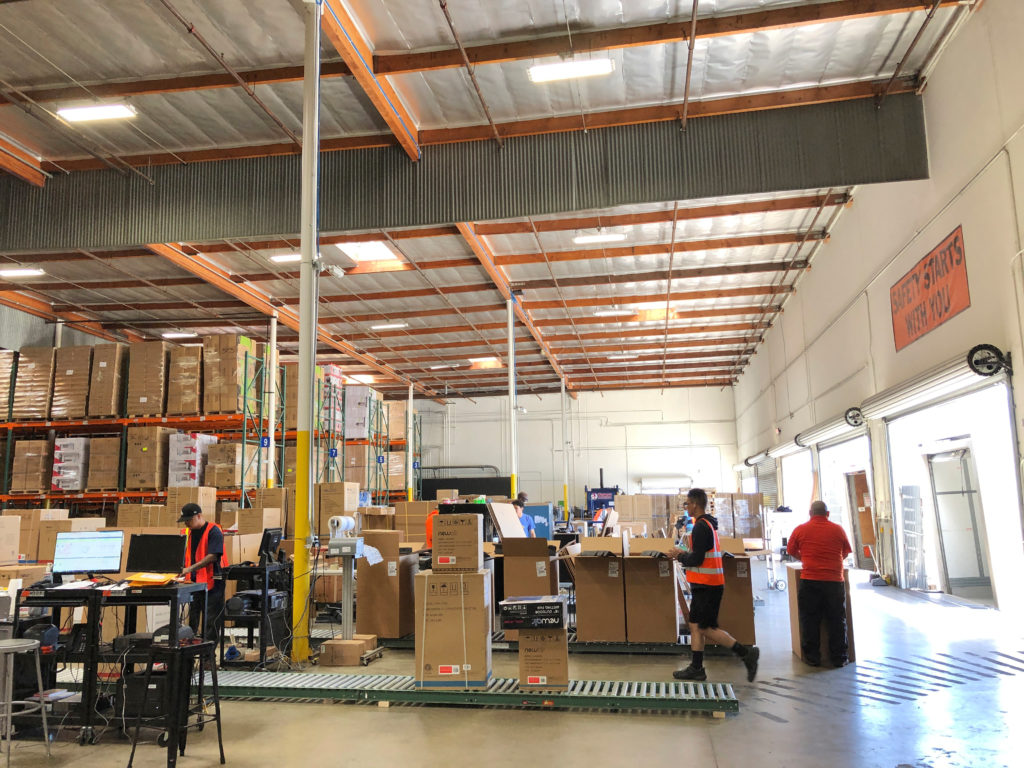A worker walks passed boxes on a roller conveyor at NewAir's warehouse in Cypress, California, U.S. on May 24, 2019. Pictu...