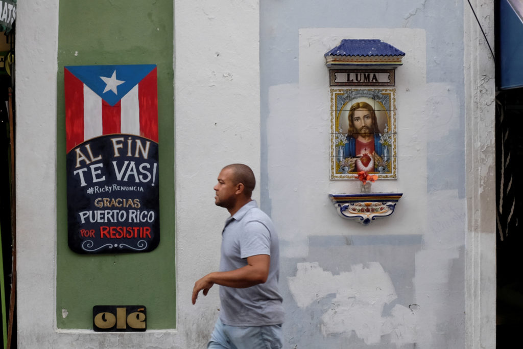 A man walks past a sign that reads "You are finally leaving. Ricky resign. Thanks Puerto Rico for resisting" on the street...