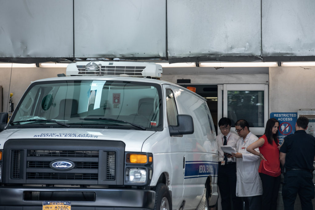 Hospital staff work on paperwork next to a medical examiner car outside New York Presbyterian-Lower Manhattan Hospital, wh...