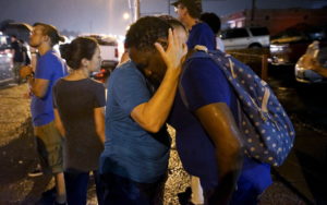 A white woman holds a black woman as they pray during a rain storm at the site of last year's riots on the one year anniversary of the killing of Michael Brown in Ferguson