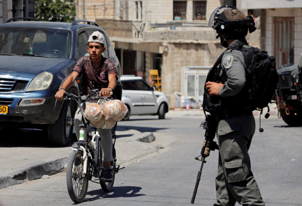 A Palestinian boy rides a bicycle past an Israeli border policeman during a raid after the Israeli military said an Israel...