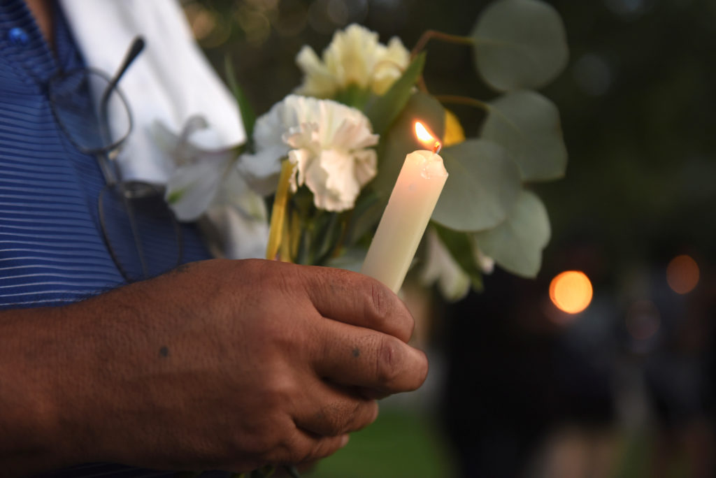 A man holds flowers and a candle as people gather for a vigil following Saturday's shooting in Odessa, Texas, on September...